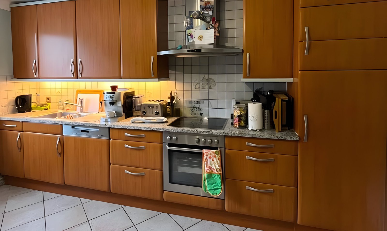 Avant : cuisine linéaire aux façades en bois orangé miel, crédence en carrelage blanc et plan de travail en granit.