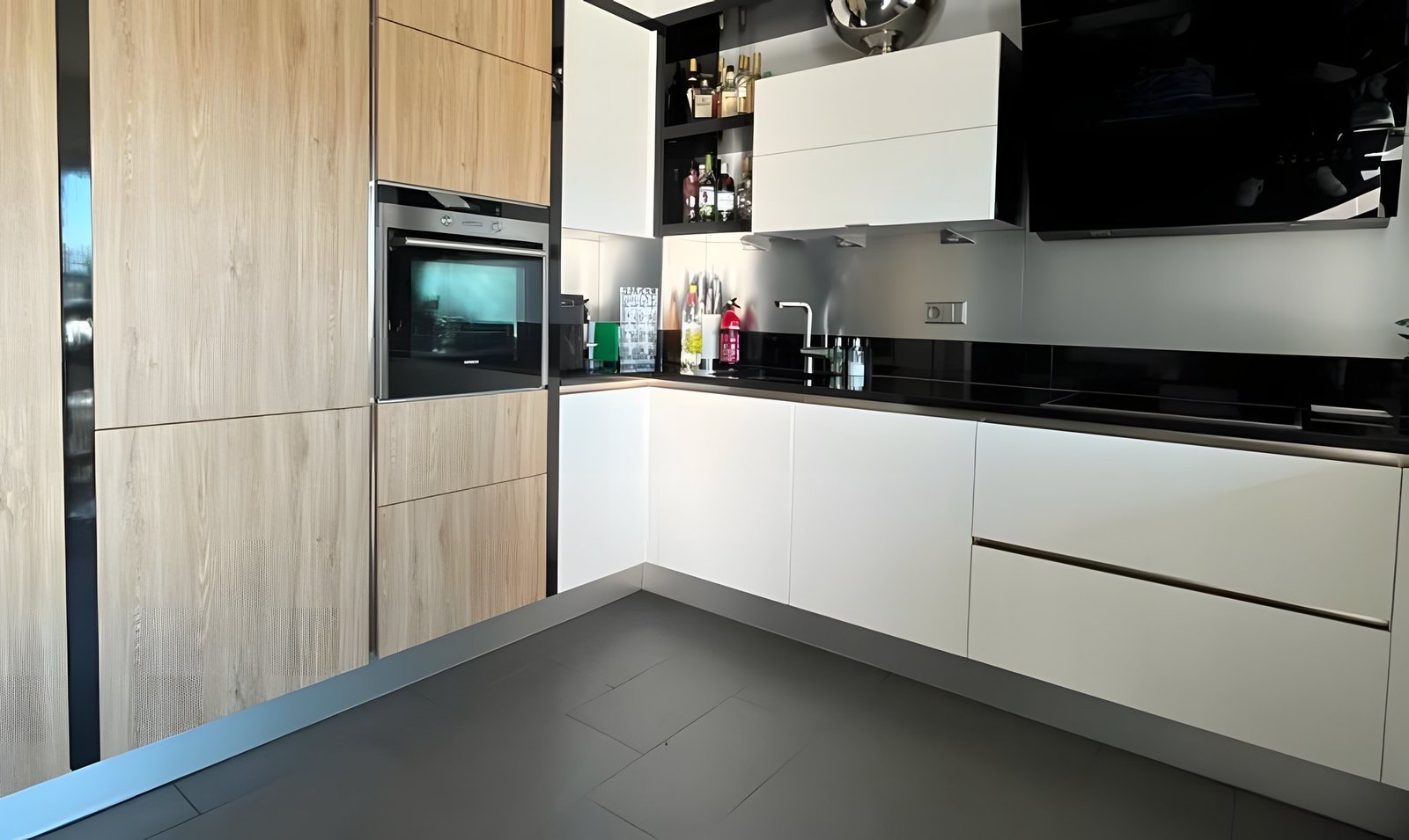 Après : la même cuisine avec des colonnes aspect chêne clair et des meubles blanc mat, plan de travail noir conservé.