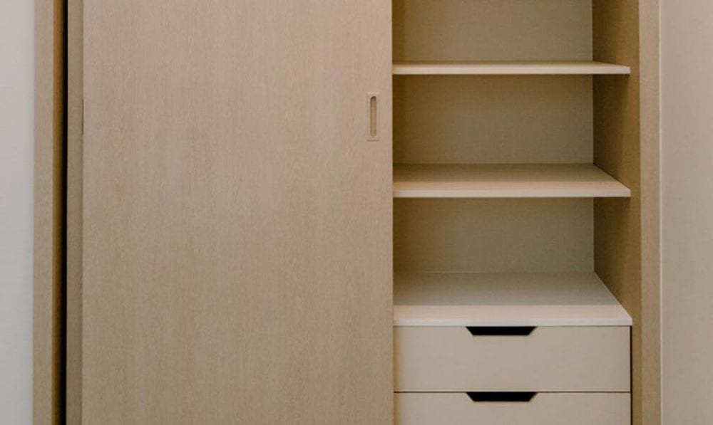 Après : la même armoire aspect chêne clair avec porte coulissante pleine, étagères et tiroirs.