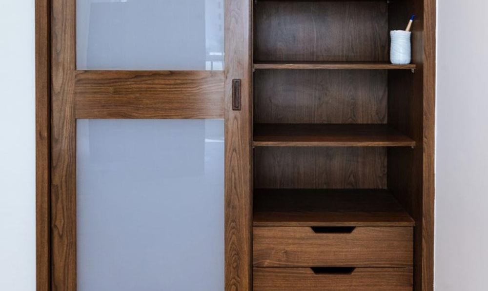 Avant : armoire aspect noyer brun foncé avec porte coulissante à verre dépoli, étagères et tiroirs.
