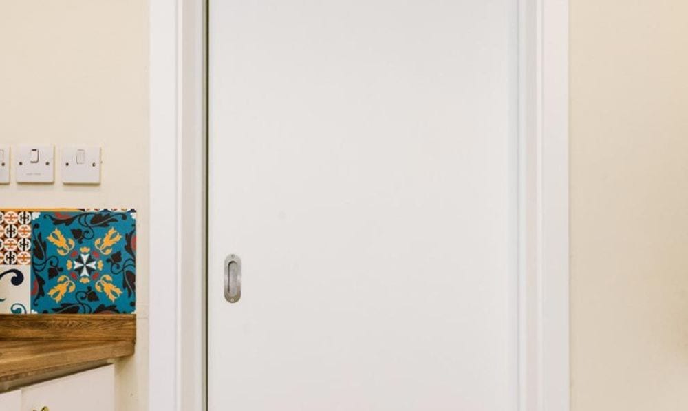 Après : la même porte coulissante en blanc mat avec chambranle blanc, à côté d'un plan de travail en bois.