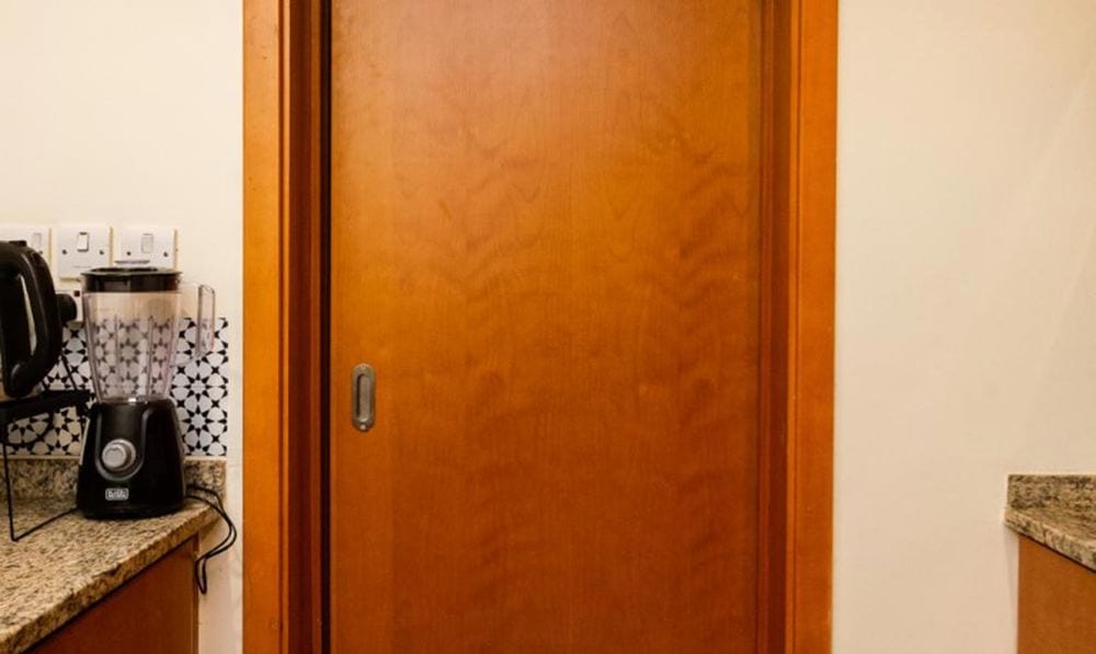 Avant : porte coulissante en bois orangé verni avec chambranle assorti, à côté d'un plan de travail en granit.