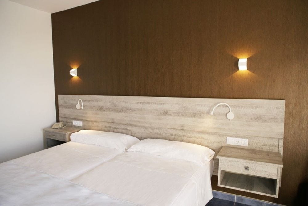 Après : la même chambre avec tête de lit et chevets aspect bois clair vieilli devant un mur brun texturé.